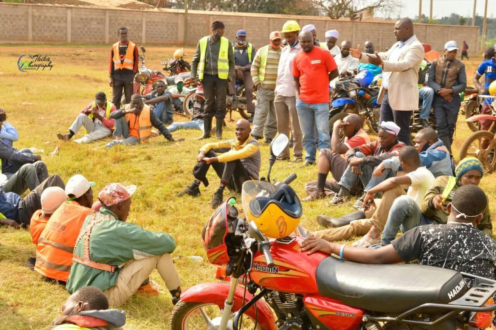 A community baraza in Thika with boda boda riders seated on the grass